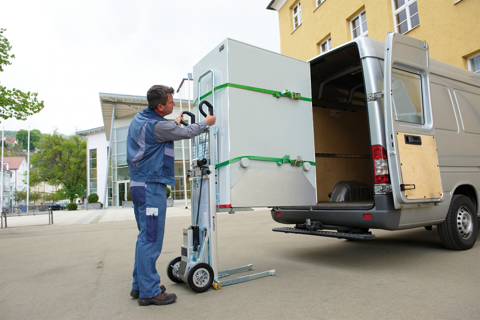 Das Bild zeigt einen Mann, der einen CargoMaster Treppensteiger für Lasten verwendet, um eigenständig eine große Maschine in einen Van zu laden, ohne zusätzliche Hilfe