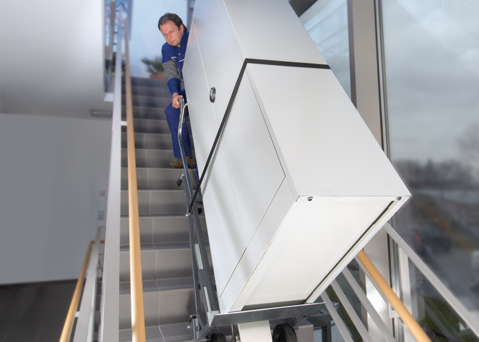Das Bild zeigt den Einsatz des CargoMaster Treppensteigers mit einem großen Schrank, welcher in einer Stadthalle über moderne Treppen transportiert wird.